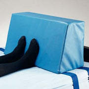 Blue foam wedge used as a footrest on a bed with black socks.