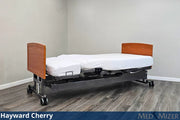 Electric hospital bed with wooden head and footboards on a gray floor.