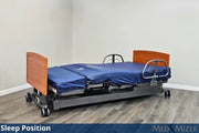 Elevated hospital bed with wooden headboard and footboard on a wooden floor.