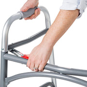 Person using a silver walker with red handle on a white background