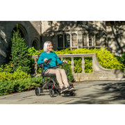 Woman using a mobility scooter outdoors with a building and greenery in the background