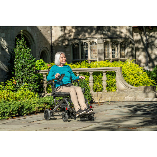 Woman using a mobility scooter outdoors with a building and greenery in the background