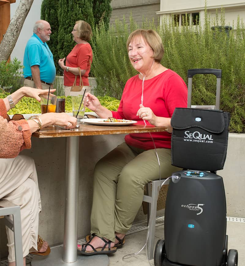 Woman sitting at an outdoor table with a Sequal air purifier on wheels.