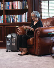 Woman knitting on a brown leather couch with a bookshelf in the background