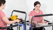 Two women using adjustable height tables with handles in a clinical setting.