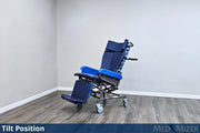 A blue and black tilt-in-position wheelchair shown in a corner room with gray walls and wood-look flooring, with text overlays reading 'Tilt Position' and 'MED MIZER'.