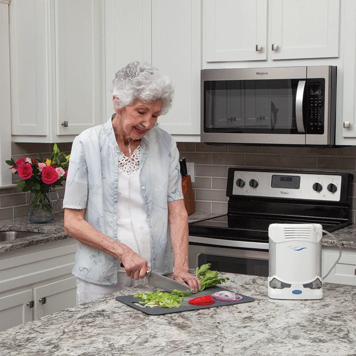 Woman preparing food in a kitchen with a portable air concentrator on the counter.
