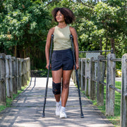 Woman using crutches on a wooden path with greenery in the background