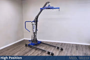 A high-position medical lift chair with a blue base and arm, gray frame, and black wheels, shown in a room corner with gray walls and wood-look flooring. A blue banner at the bottom reads 'High Position' and 'MED MIZER'.