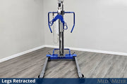 A blue and silver medical lift with a wheeled base stands in a room corner with gray wood-look flooring and light gray walls. The lift is shown with its legs retracted, and text overlays at the bottom read 'Legs Retracted' and 'MED MIZER'.