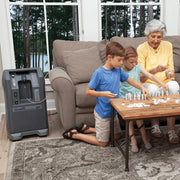 Three people playing a board game in a living room with a home oxygen concentrator.
