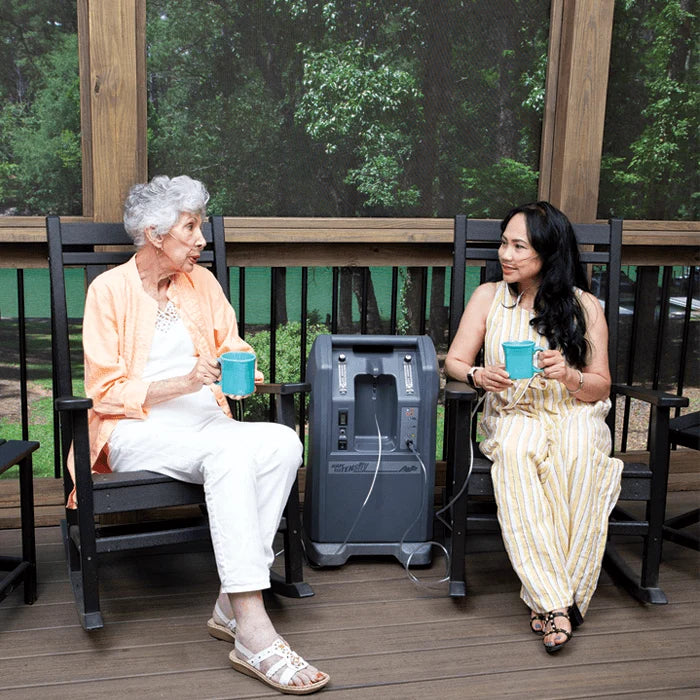 Two women sitting on a wooden deck with a portable power station between them.