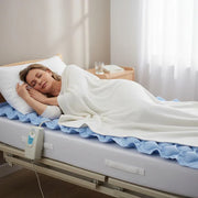 Woman lying in bed with a medical mattress pad in a bright room.