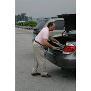 Man loading a suitcase into the trunk of a car in a parking lot.