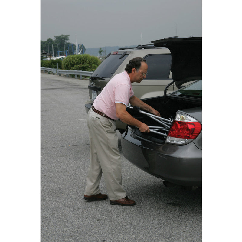 Man loading a suitcase into the trunk of a car in a parking lot.