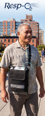 A man outdoors wearing a Resp-O2 portable oxygen concentrator on his chest, with a nasal oxygen tube connected. The device is a black rectangular unit with tubing and a small screen, worn in a black pouch across his chest.
