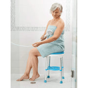 Woman using a handheld showerhead on a stool in a bathroom.