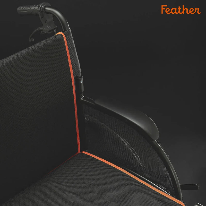 Black wheelchair with orange accents on a dark background, featuring the brand 'Feather'.