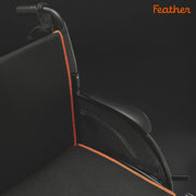 Black wheelchair with orange accents on a dark background, featuring the brand 'Feather'.