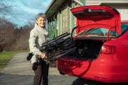 Woman loading folded bike into a red car trunk outdoors.