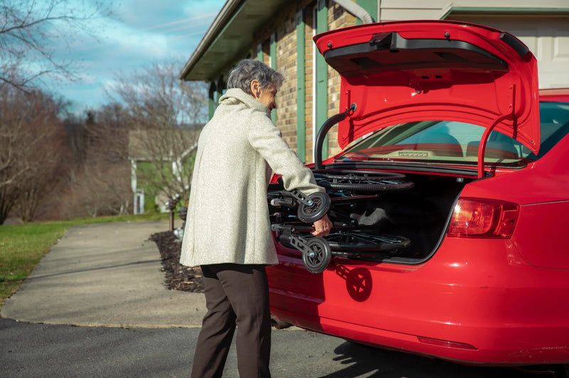 Person loading items into the trunk of a red car outdoors.