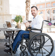 Man in a wheelchair using a laptop outdoors