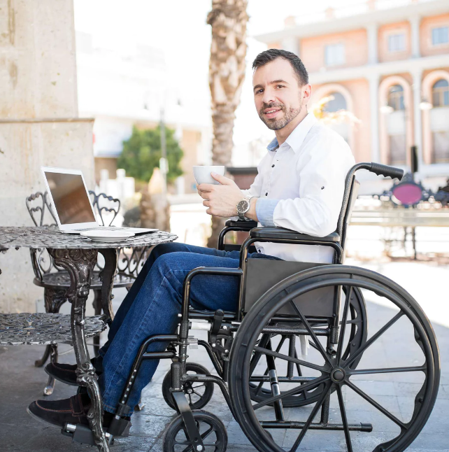 Man in a wheelchair using a laptop outdoors