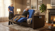 A man reclines in a blue and dark wood motorized lounge chair in a cozy living room, while a woman stands nearby holding a remote control.