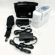 A portable oxygen concentrator kit laid out on a white background, including a white and blue concentrator unit, black carrying bag, black power adapters, a black car power cable, a black strap, and small white replacement parts.