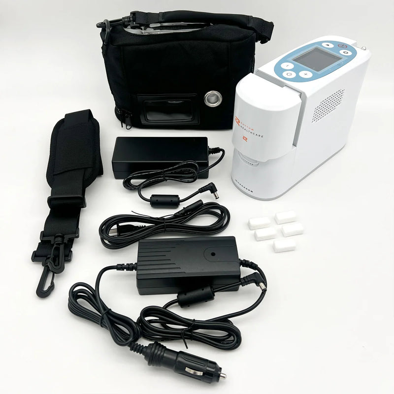 A portable oxygen concentrator kit laid out on a white background, including a white and blue concentrator unit, black carrying bag, black power adapters, a black car power cable, a black strap, and small white replacement parts.