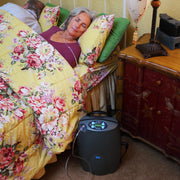 Woman sleeping on a bed with floral bedding next to an air purifier on the floor.