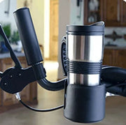 Stainless steel travel mug attached to a bicycle handlebar with a blurred indoor background.