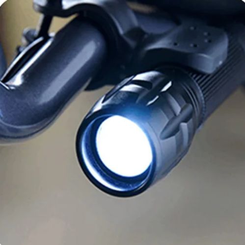 Close-up of a flashlight attached to a motorcycle handlebar.