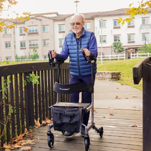 Man using a walker outdoors on a wooden deck with apartment buildings in the background