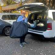 Person holding a large gray bag next to an open car trunk with groceries.
