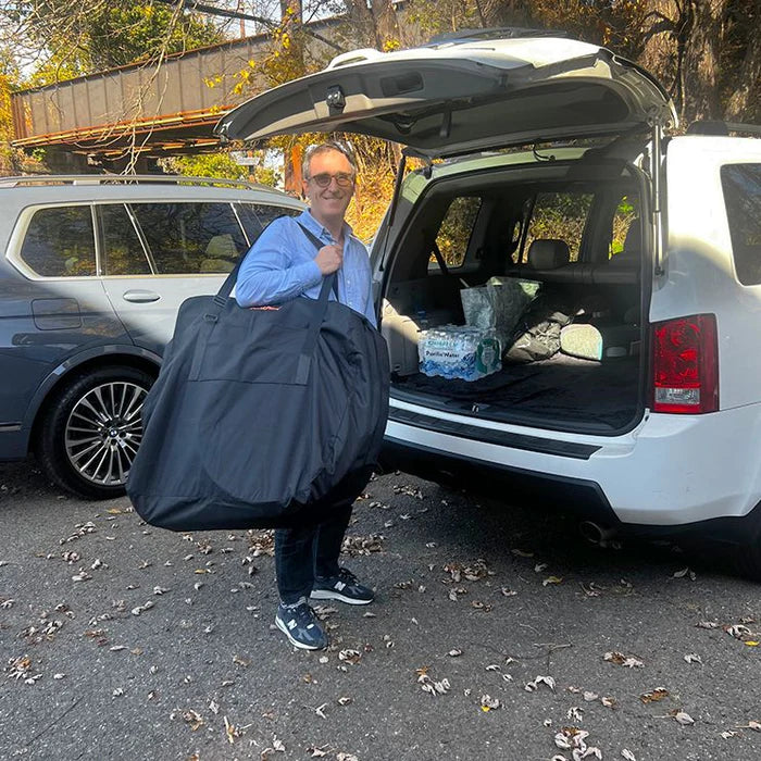 Person holding a large gray bag next to an open car trunk with groceries.
